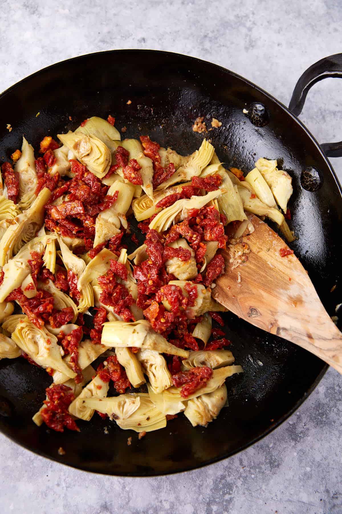 Sun-dried tomatoes added to artichokes in a skillet.