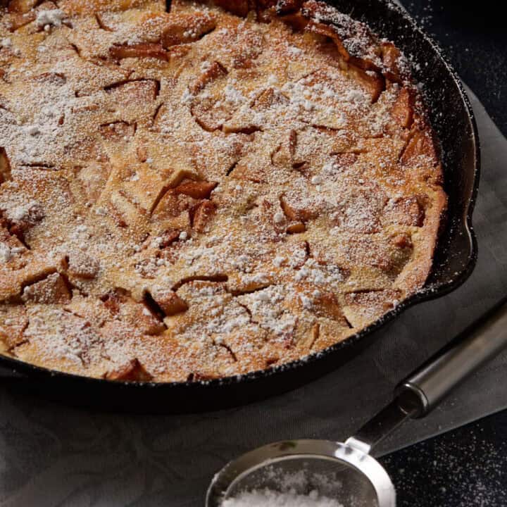 An apple pancake in a skillet with powdered sugar.
