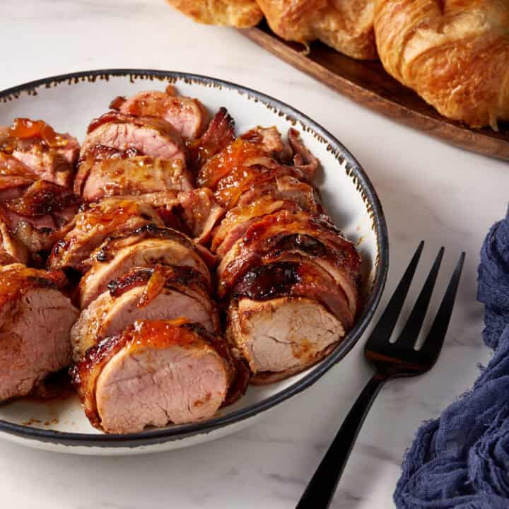 A platter of sliced pork tenderloin next to a serving fork.