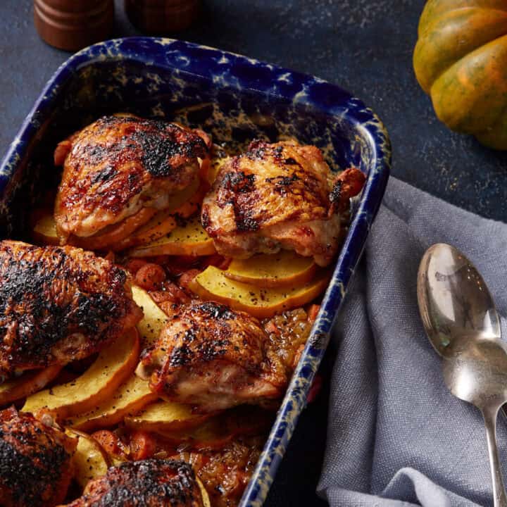 Roasted maple chicken with acorn squash in a baking dish next to serving sppons.