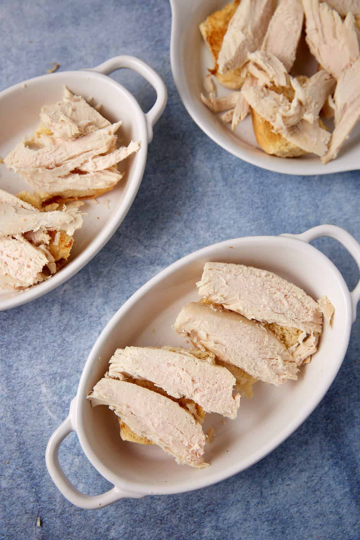 Sliced turkey on top of toasted dinner rolls.