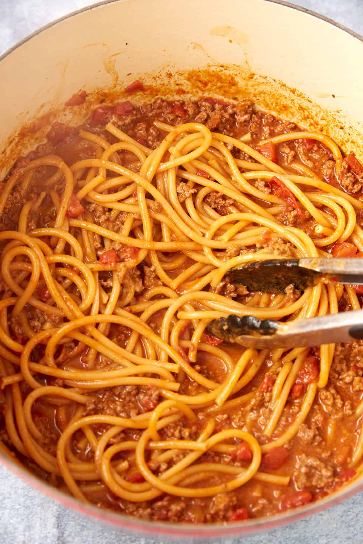 A pot of easy taco spaghetti mixed with ground meat and tomato sauce, with a pair of metal tongs resting on top of the pasta.