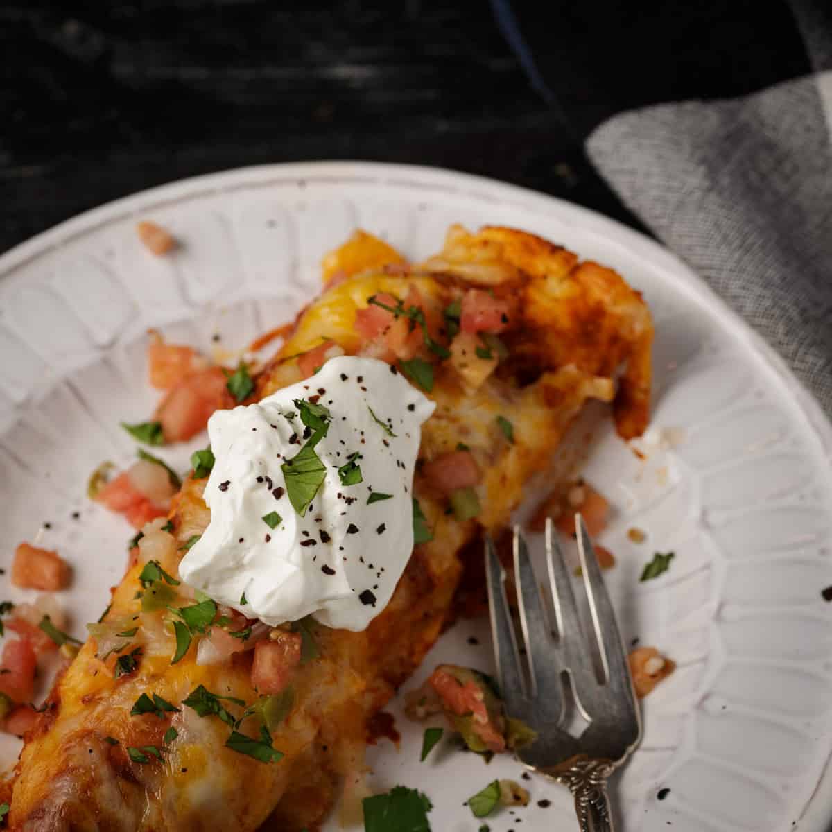 A white plate with a cheese and chicken enchilada with a fork.