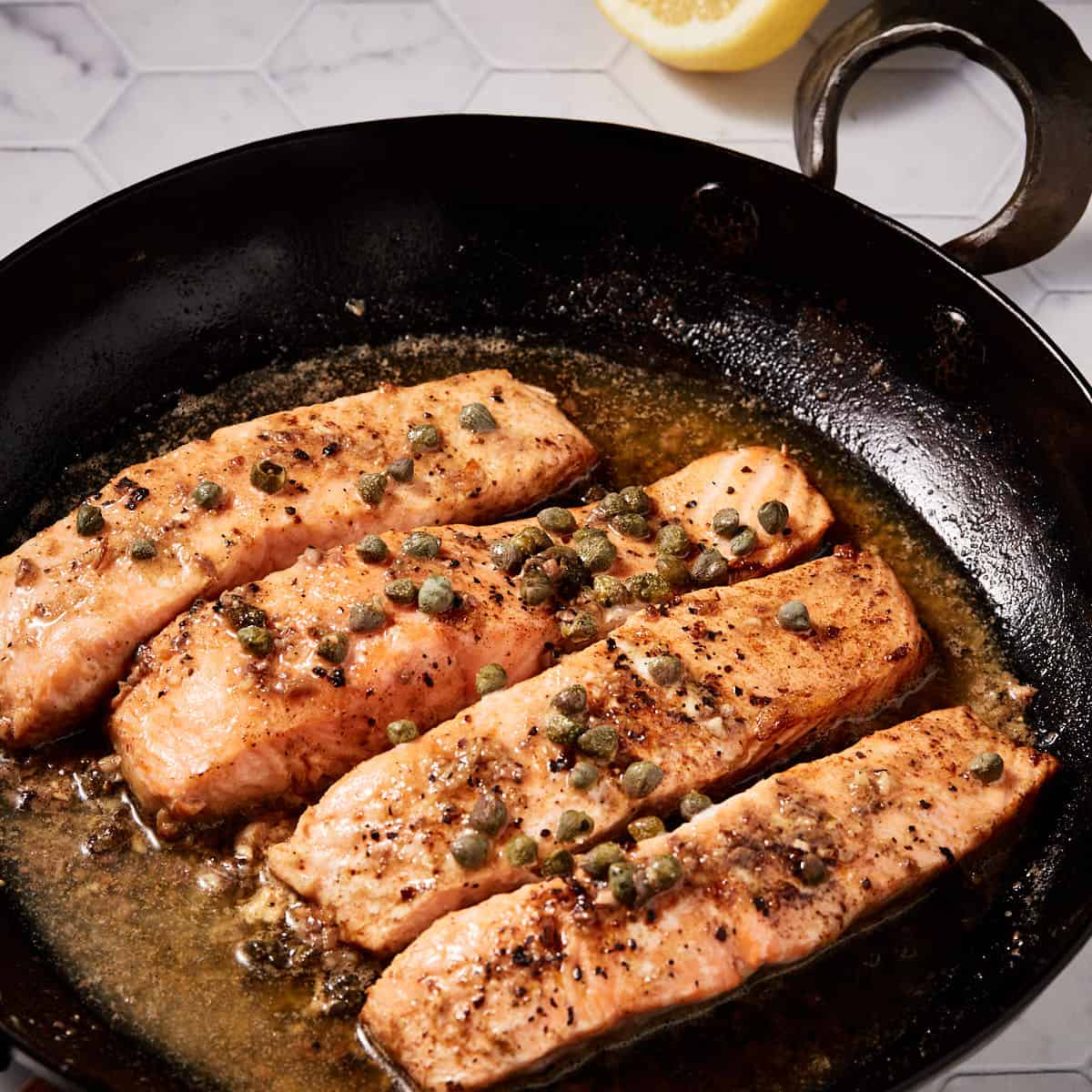 Anchovy butter all around fillets of salmon in a skillet.