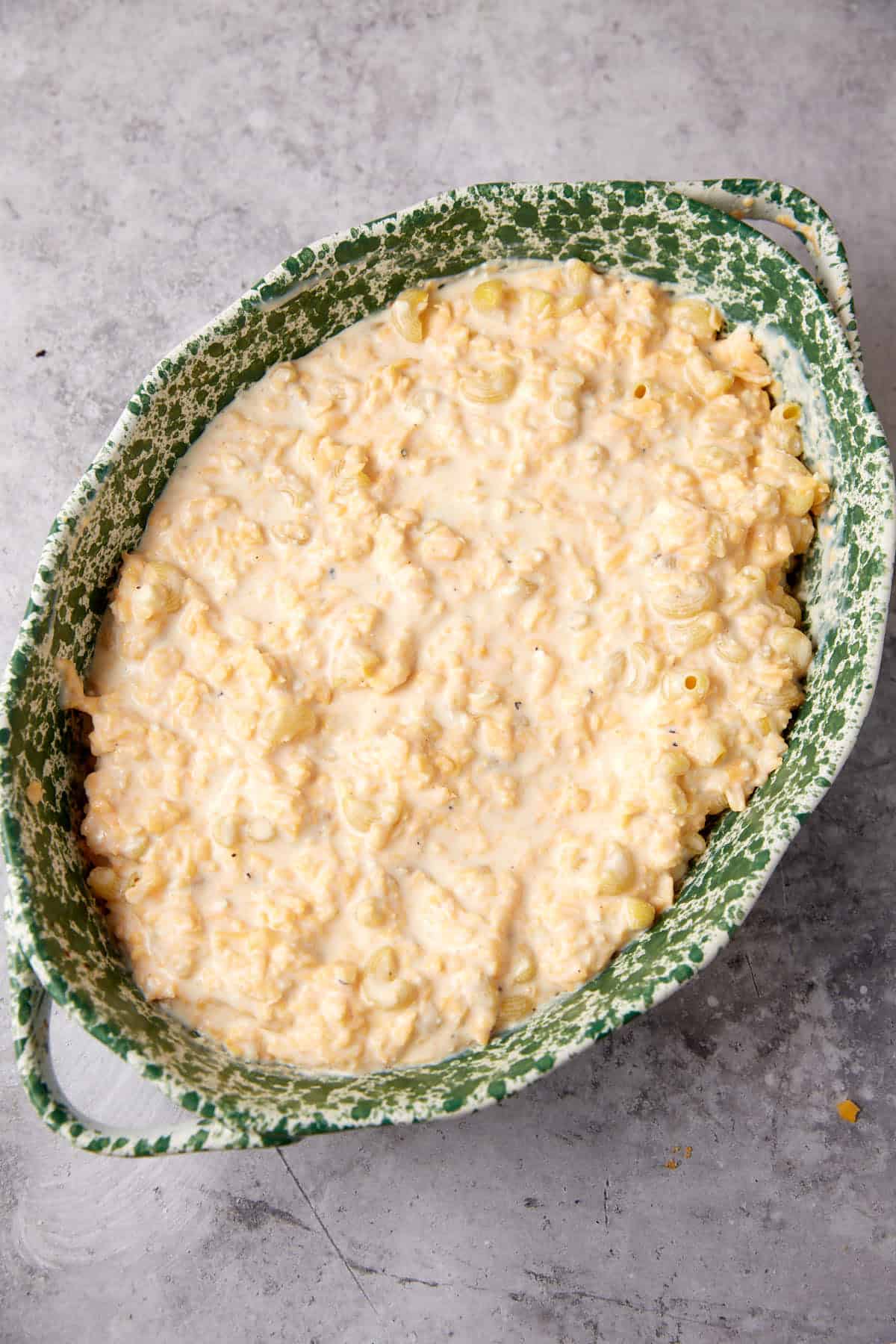 A green and white speckled baking dish filled with creamy, unbaked One Pot Macaroni and Cheese sits on a light gray countertop.