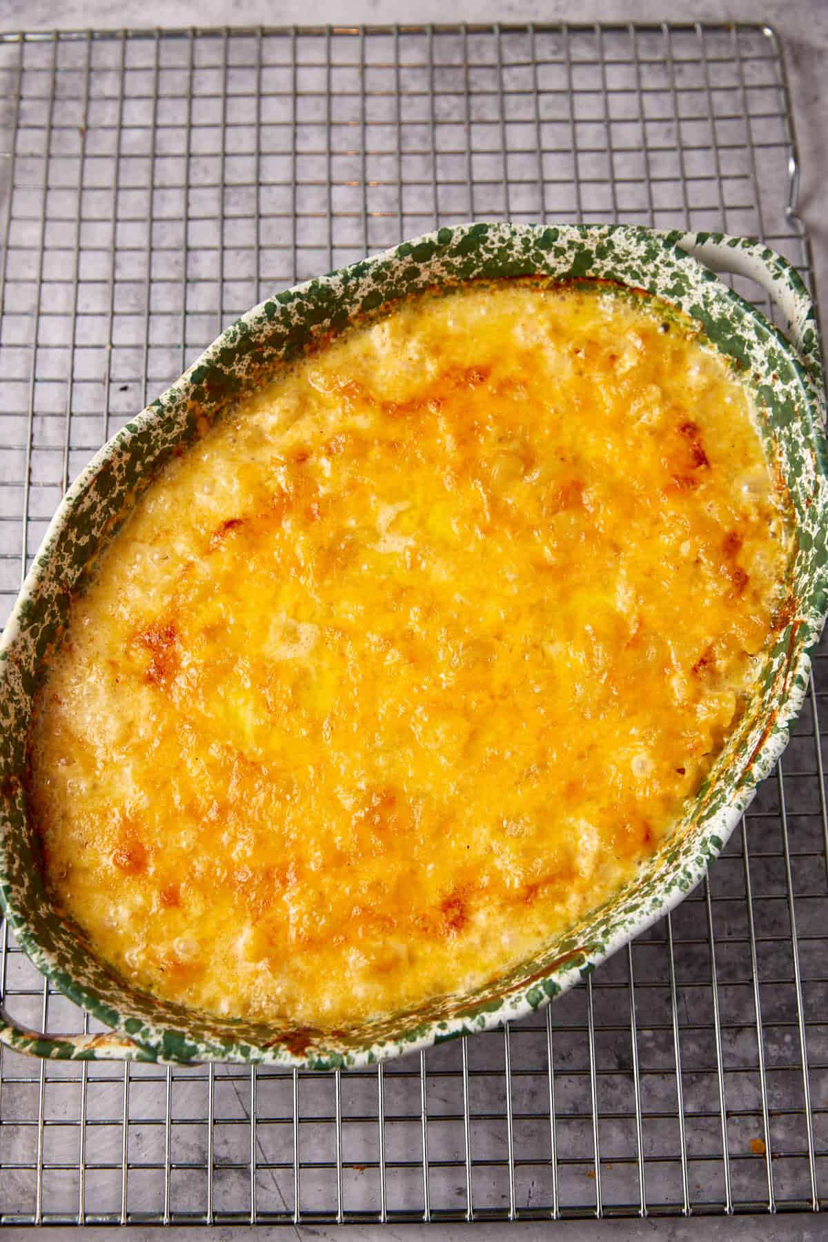 A baked casserole dish of One Pot Macaroni and Cheese features a golden, bubbly layer of melted cheese, resting on a metal cooling rack.