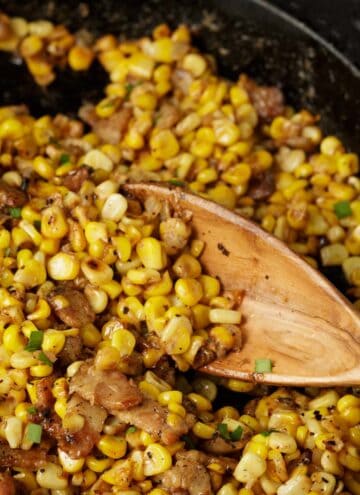 A skillet of charred corn with a wooden spoon.
