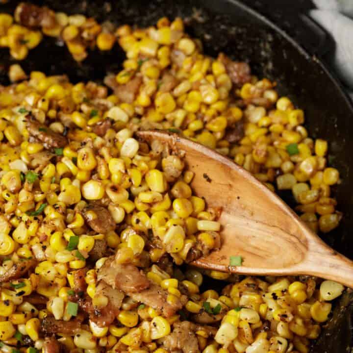 A skillet of charred corn with a wooden spoon.