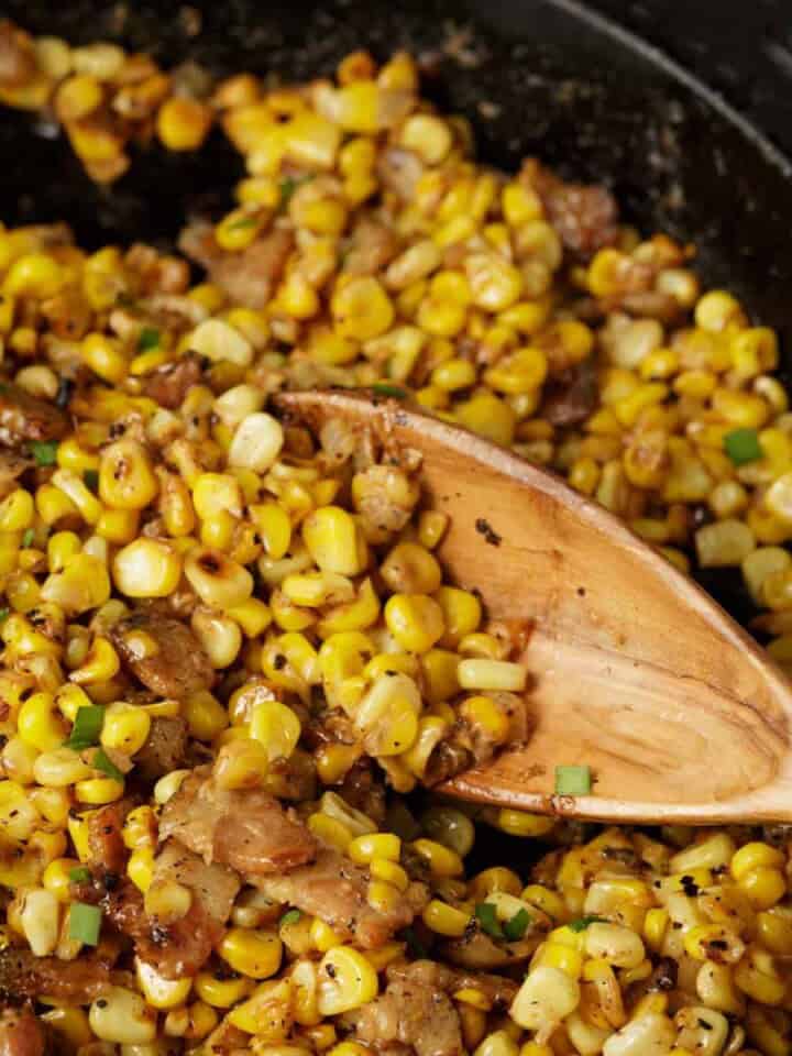 A skillet of charred corn with a wooden spoon.