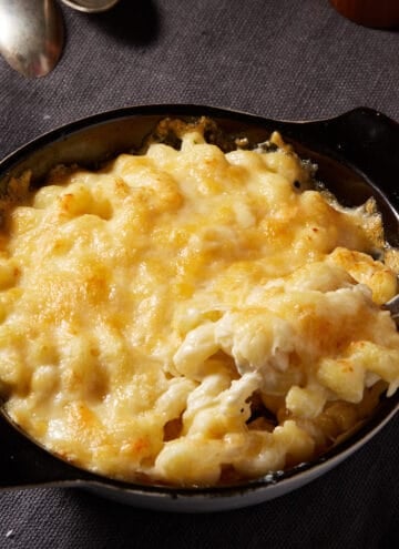 A round baking dish of mac and cheese with a serving spoon.