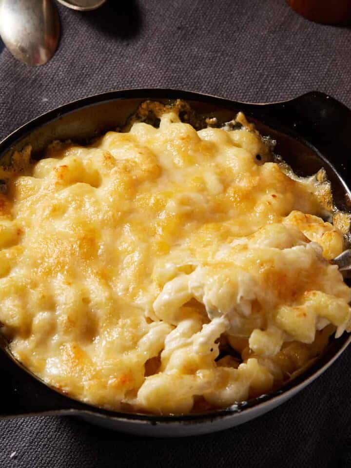 A round baking dish of mac and cheese with a serving spoon.