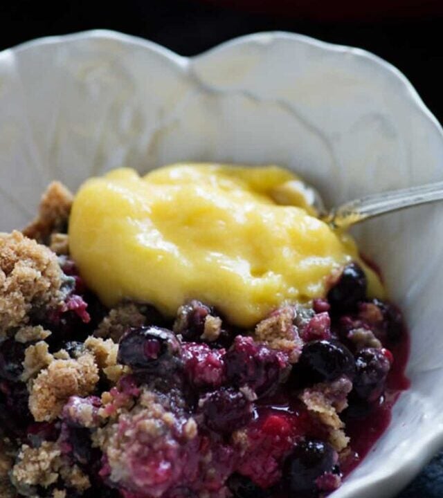 A white bowl with bumbleberry crisp topped with lemon curd.