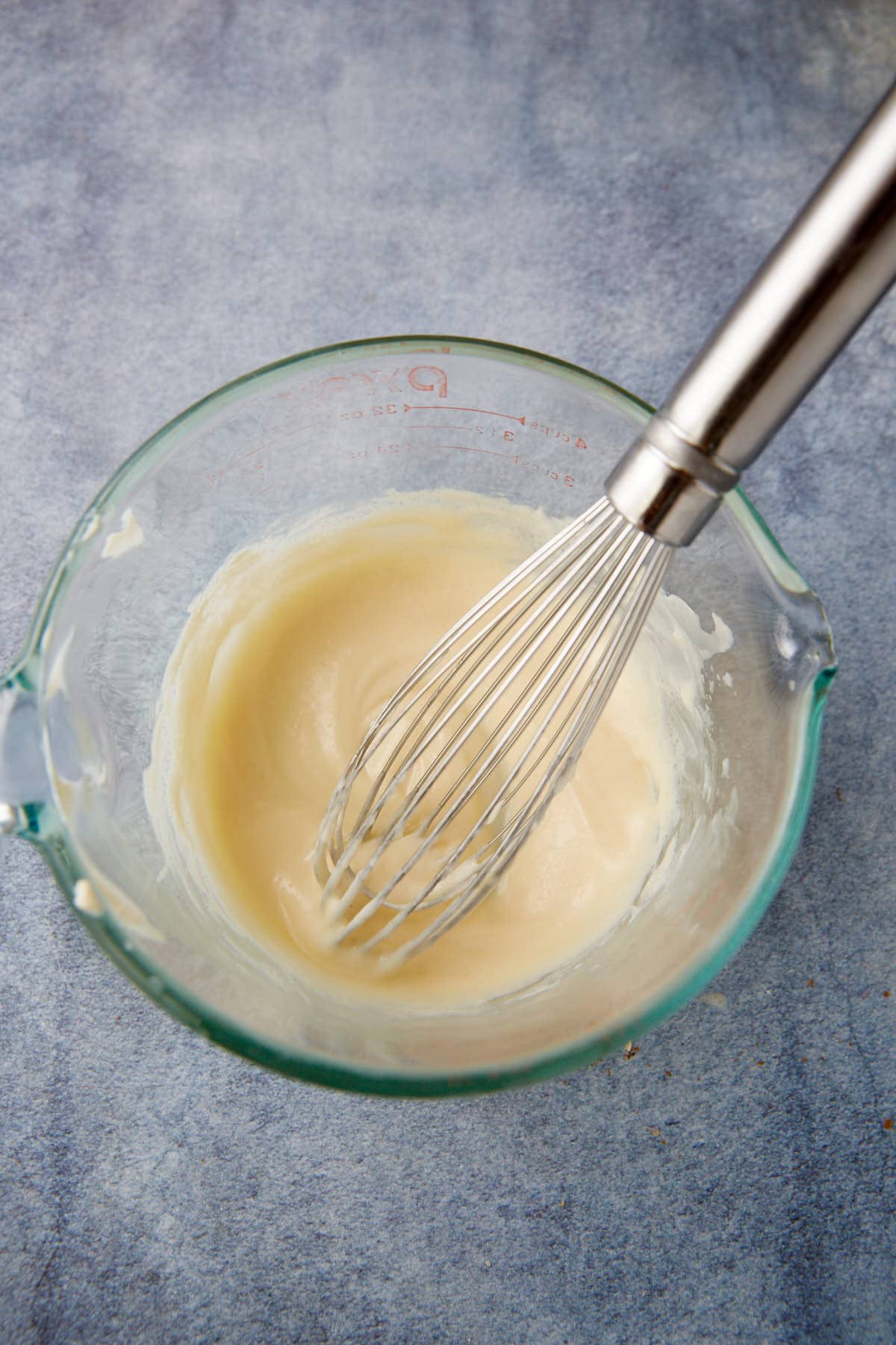 The dressing for a waldorf salad in a bowl with a whisk.
