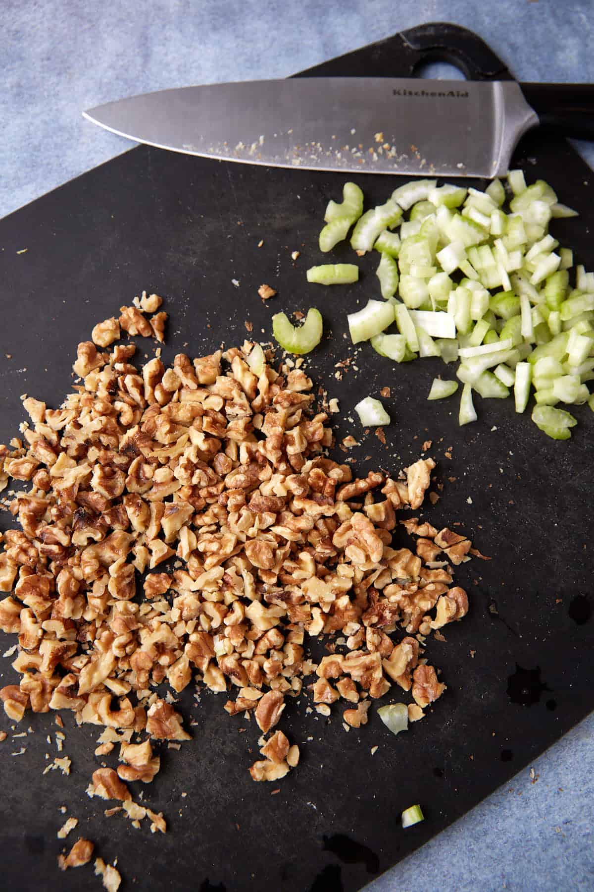 Chopped walnuts and celery on a cutting board.