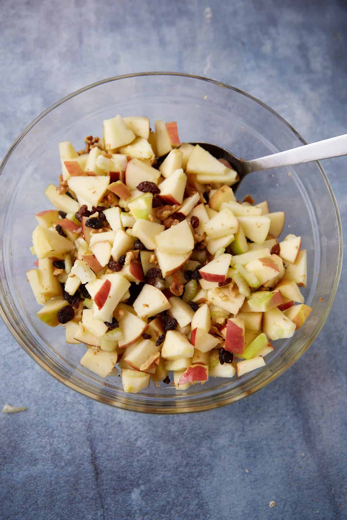 Apples being mixed with raisins, nuts and celery.