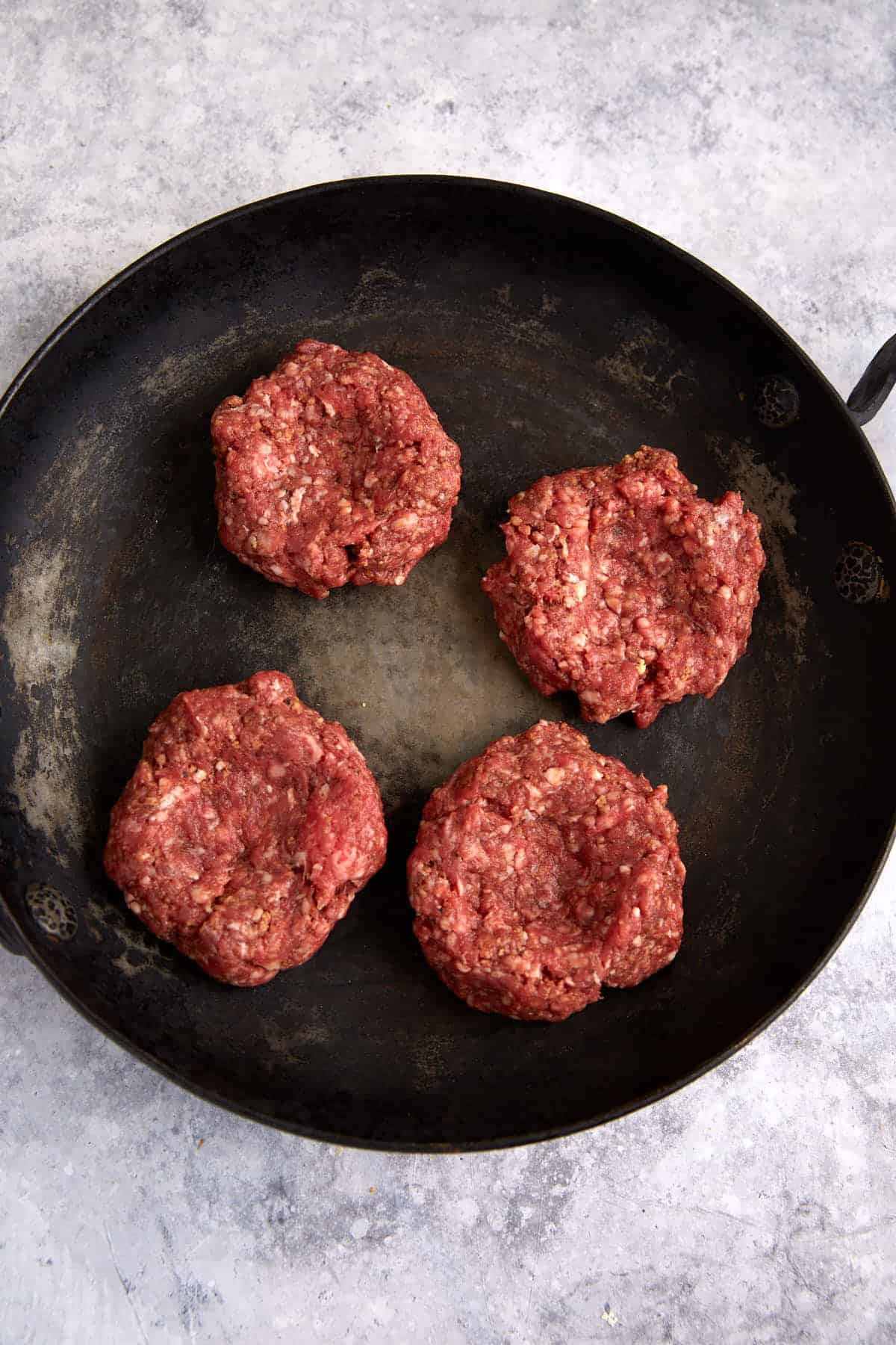 Four hamburger patties in a skillet.