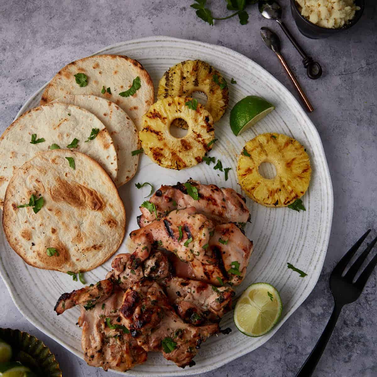 A white platter with tortillas, pineapple and grilled chicken.