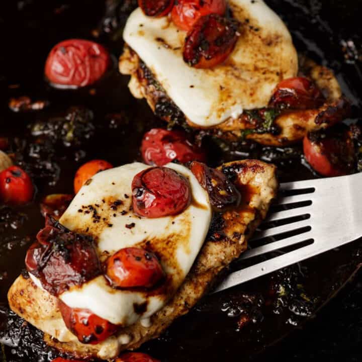 A spatula removing a serving of chicken topped with mozzarella.