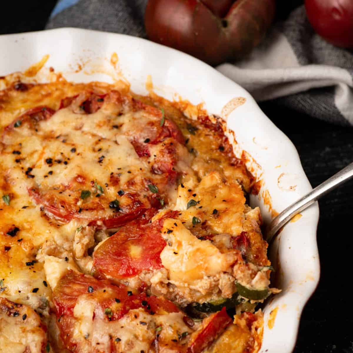 A baking dish of tomato pie with a serving spoon.