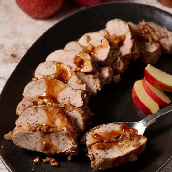 A serving of sliced pork tenderloin with apples on a serving spoon.