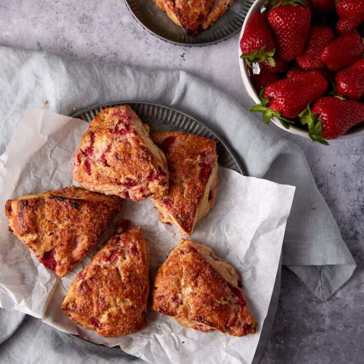 Strawberry scones on parchment paper next to a bowl of strawberries.