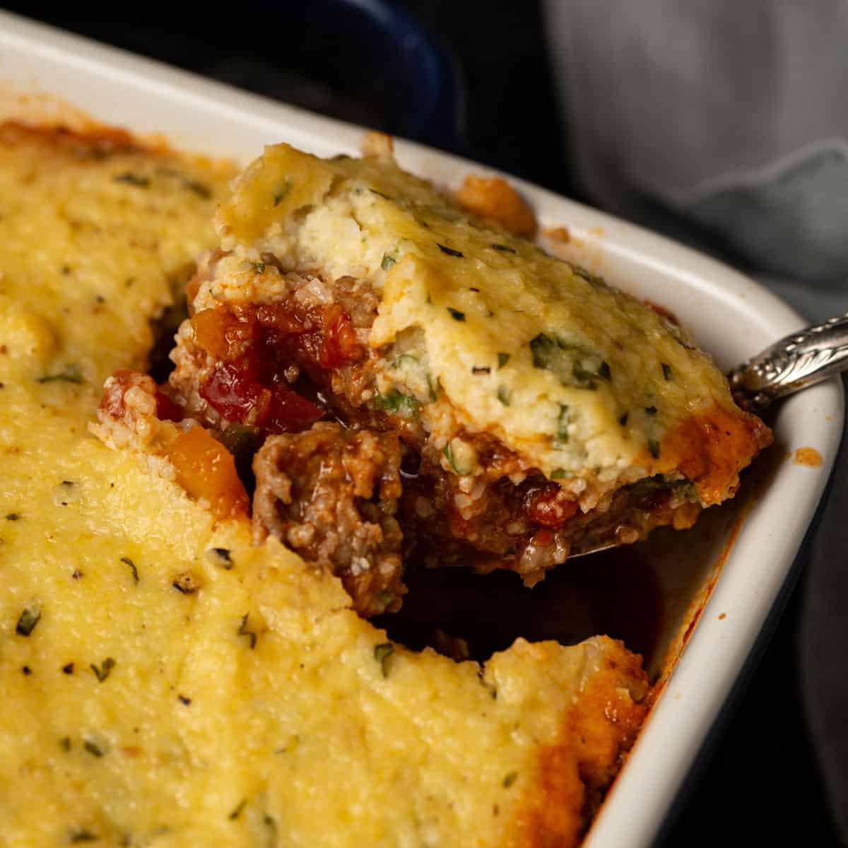 Grit topped chili casserole with a serving spoon.