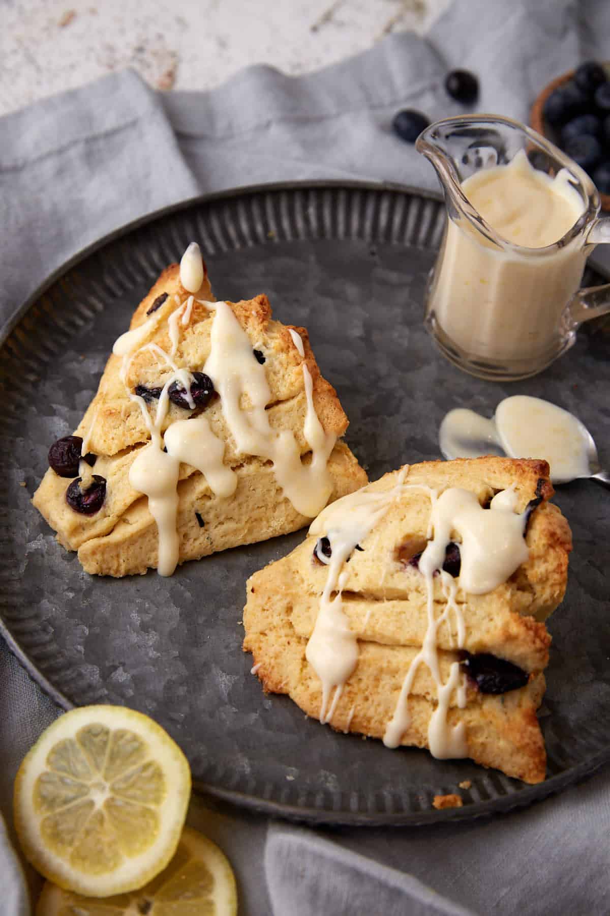 Two blueberry scones with creme fraiche next to a container of frosting.