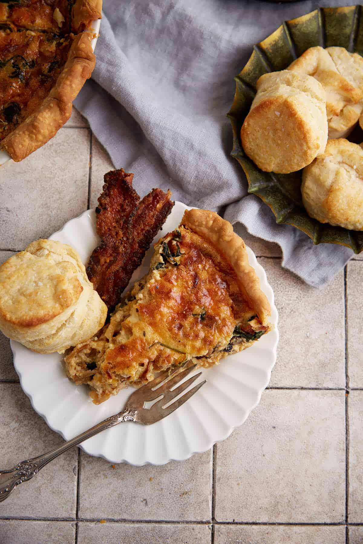 A slice of quiche next to a plate of biscuits.