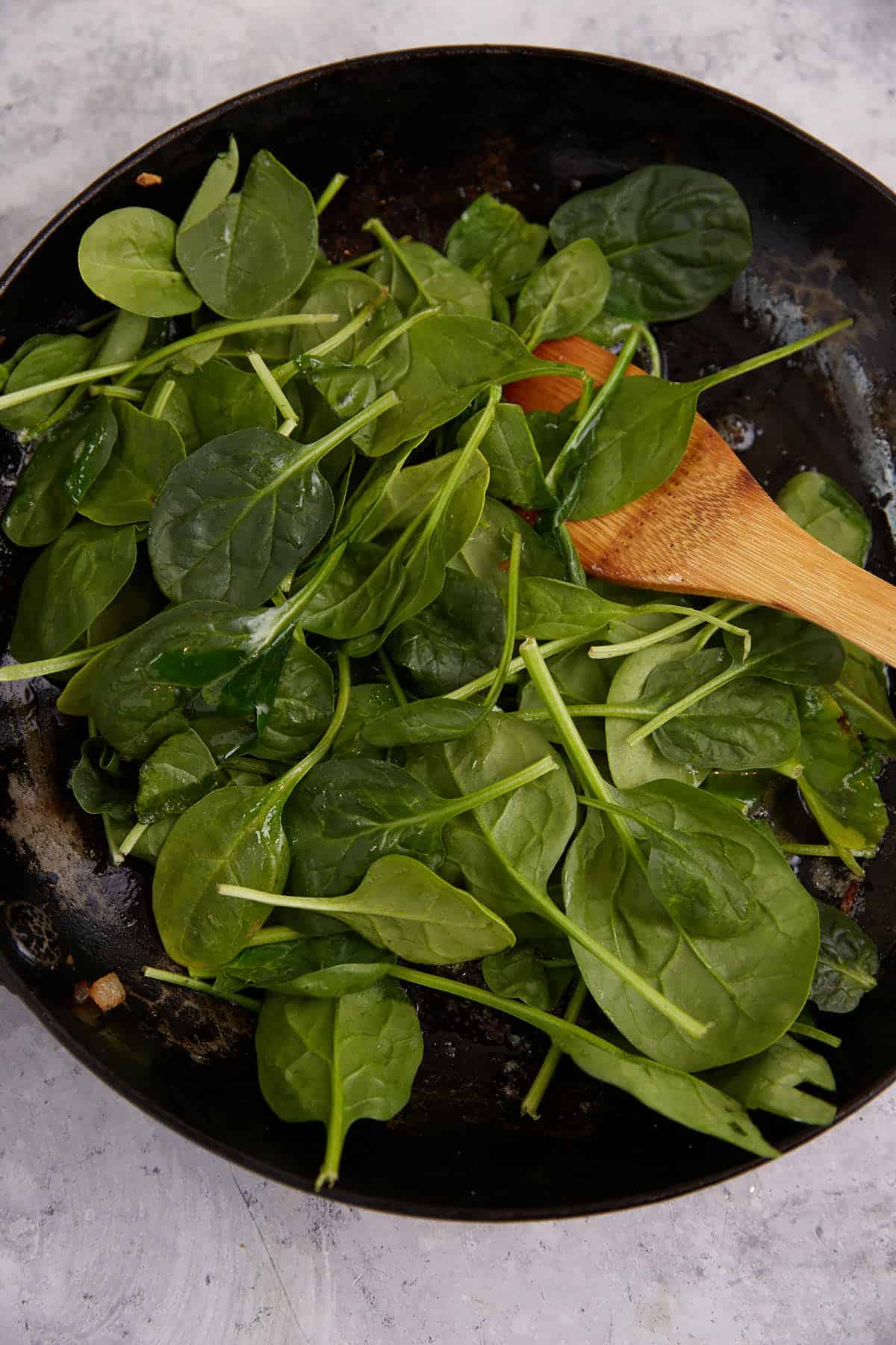 Fresh spinach added to a skillet.