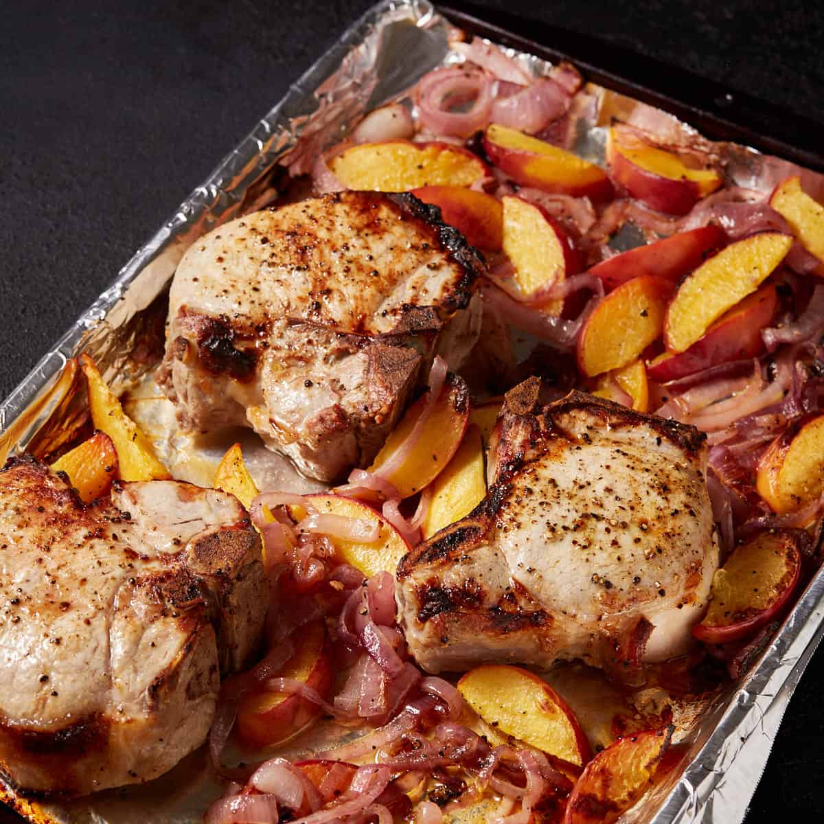 Baked peaches and pork chops on a sheet pan.