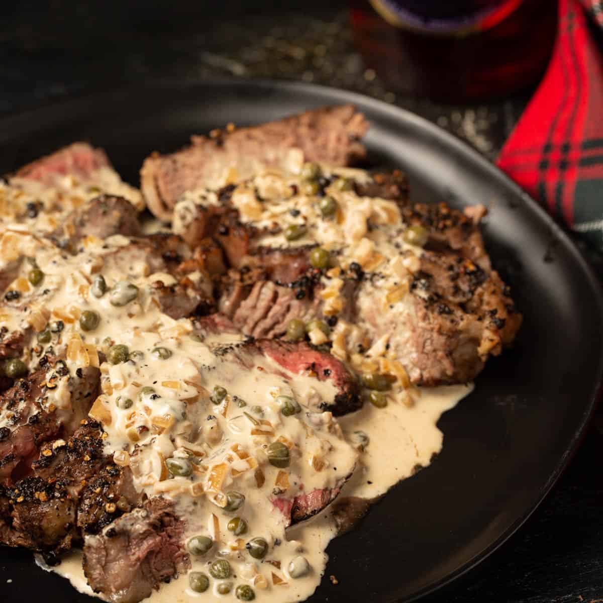 Steak covered in au poivre sauce on a platter. 