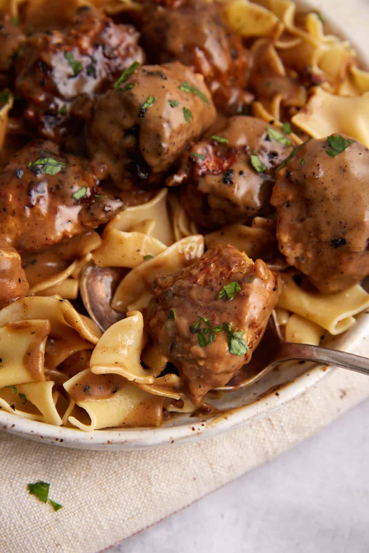 A meatball being taken out of a platter of ground chicken meatballs.