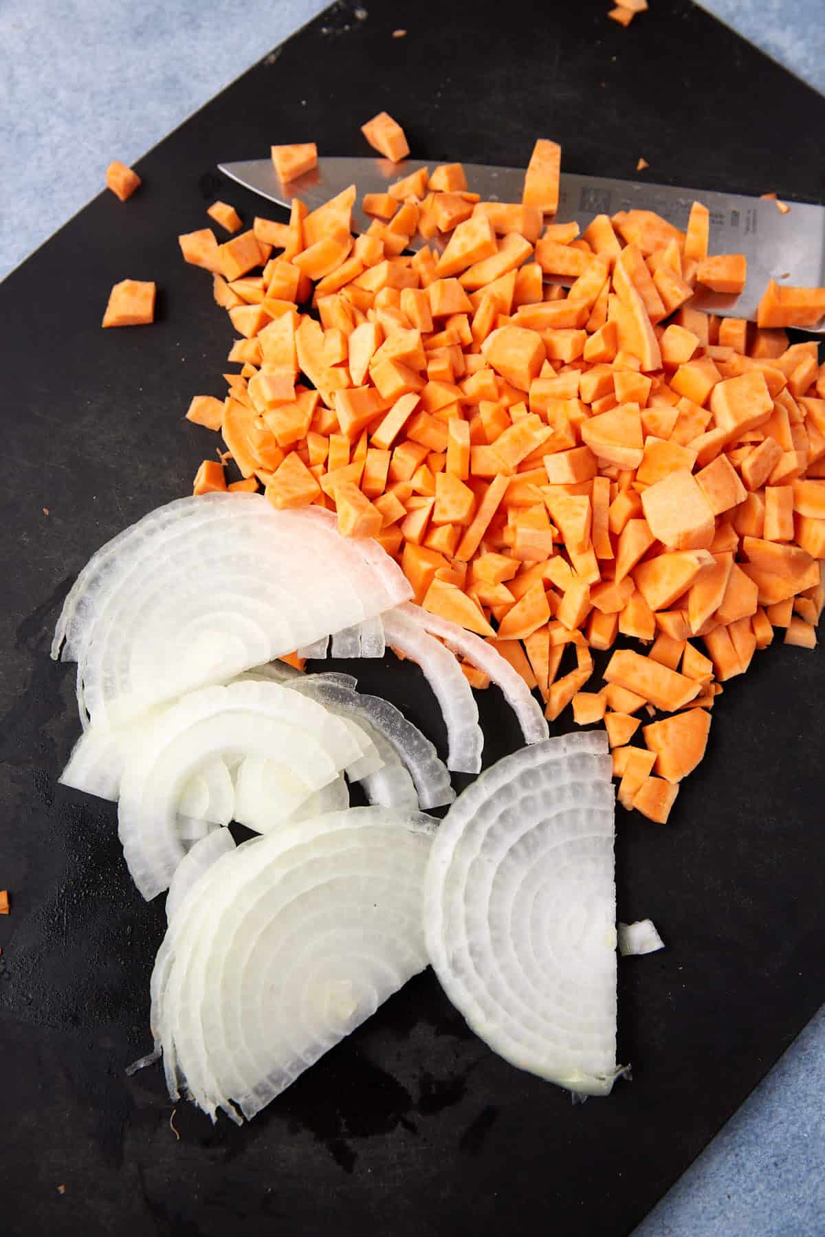 Chopped sweet potatoes and thinly sliced white onions are arranged on a black cutting board, ready to be the perfect filling for hearty Breakfast Burritos.