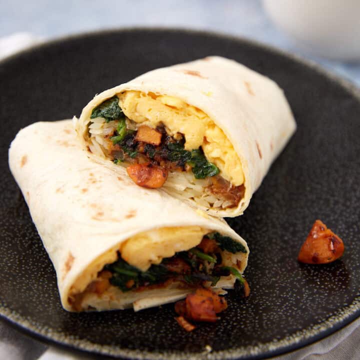 A breakfast burrito cut in half, filled with scrambled eggs, rice, sautéed vegetables, and sausage pieces, showcases why Breakfast Burritos are a hearty choice, served on a dark plate.