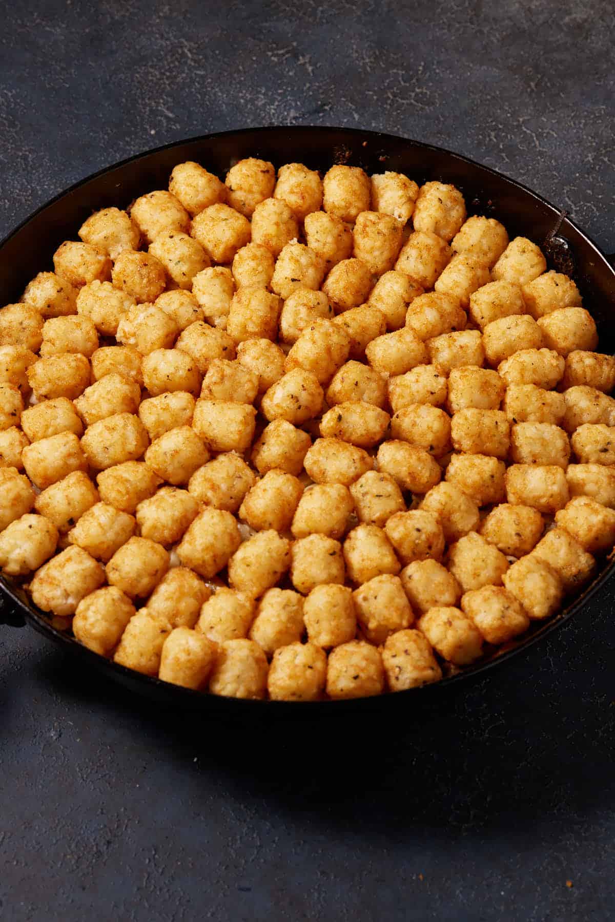 A skillet of hamburger mixture topped with tater tots.