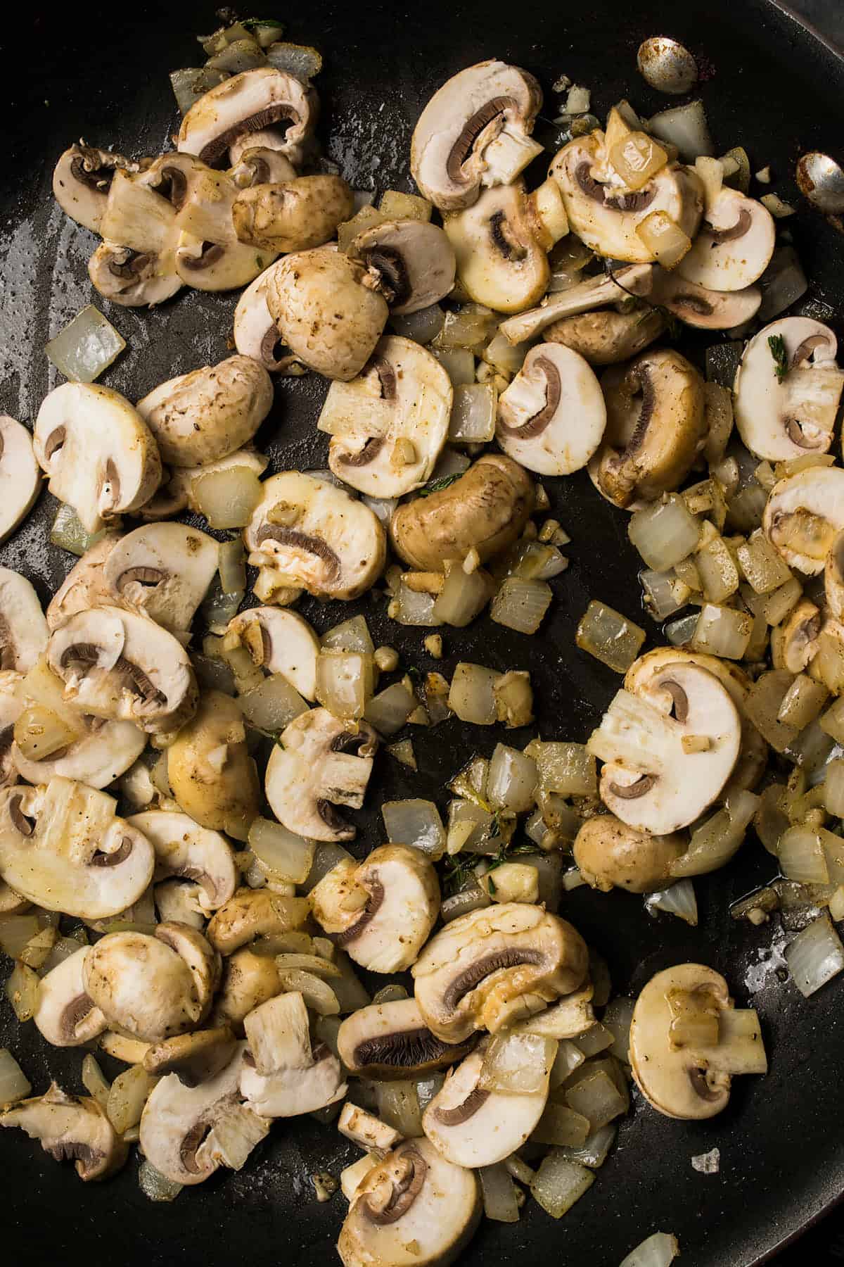 Sliced mushrooms and chopped onions sautéing in a black skillet, lightly browned and glistening with oil—perfect for a flavorful beef and Guinness pie.