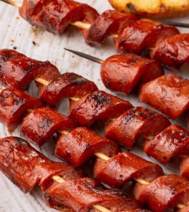 A white platter with spiral hot dogs on skewers.