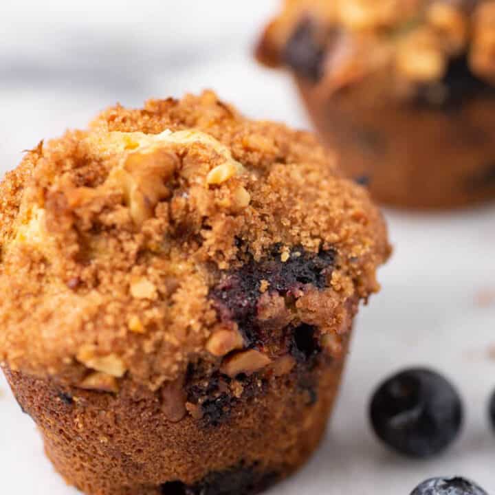 Two blueberry muffins with streusel topping on a marble board