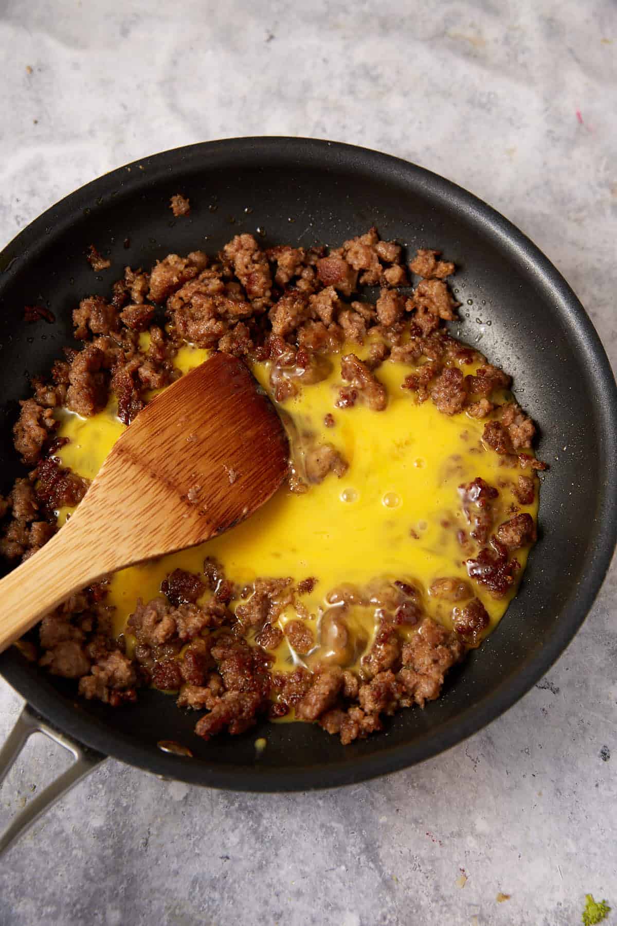 Egg added to cooked sausage in a skillet.