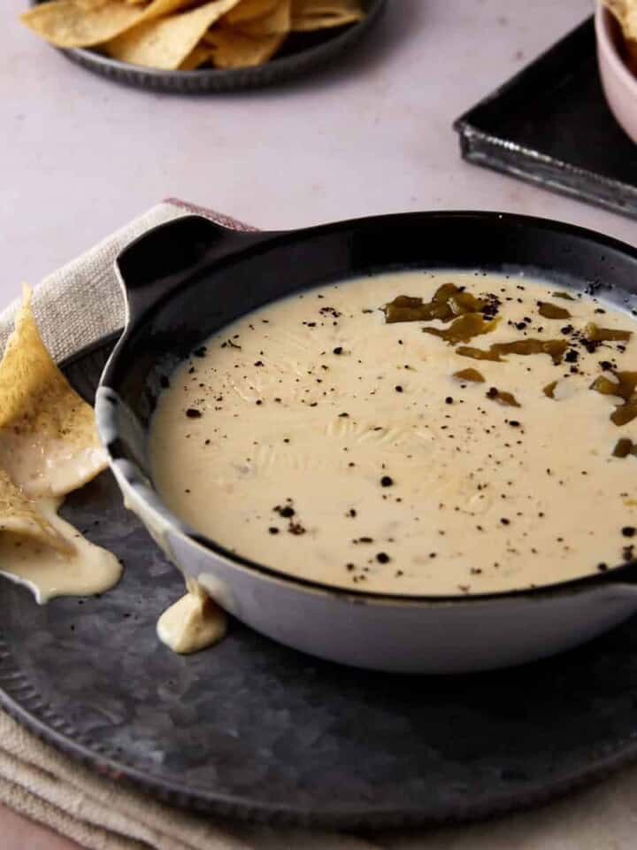 A serving bowl of homemade queso dip with tortilla chips.