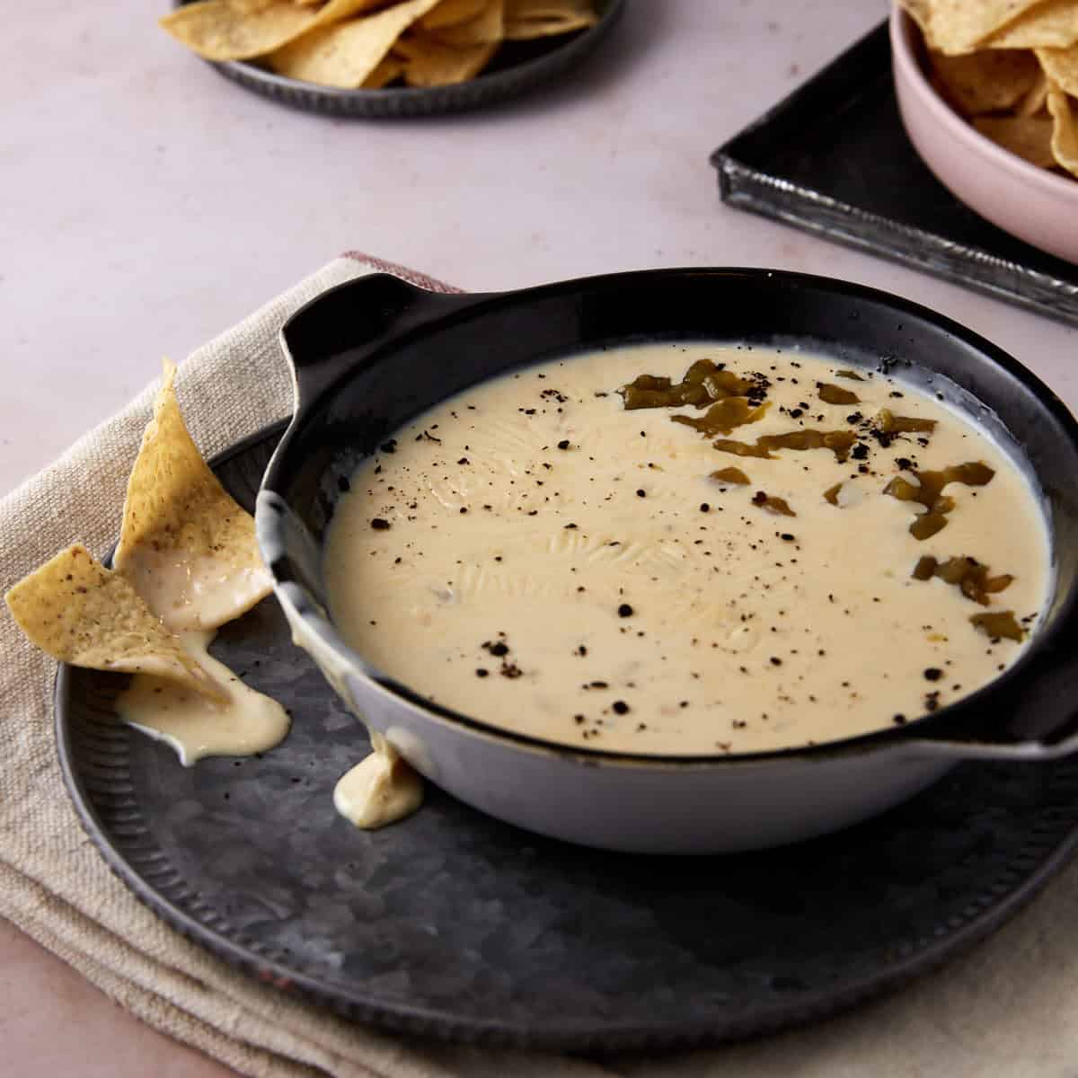 A serving bowl of homemade queso dip with tortilla chips.