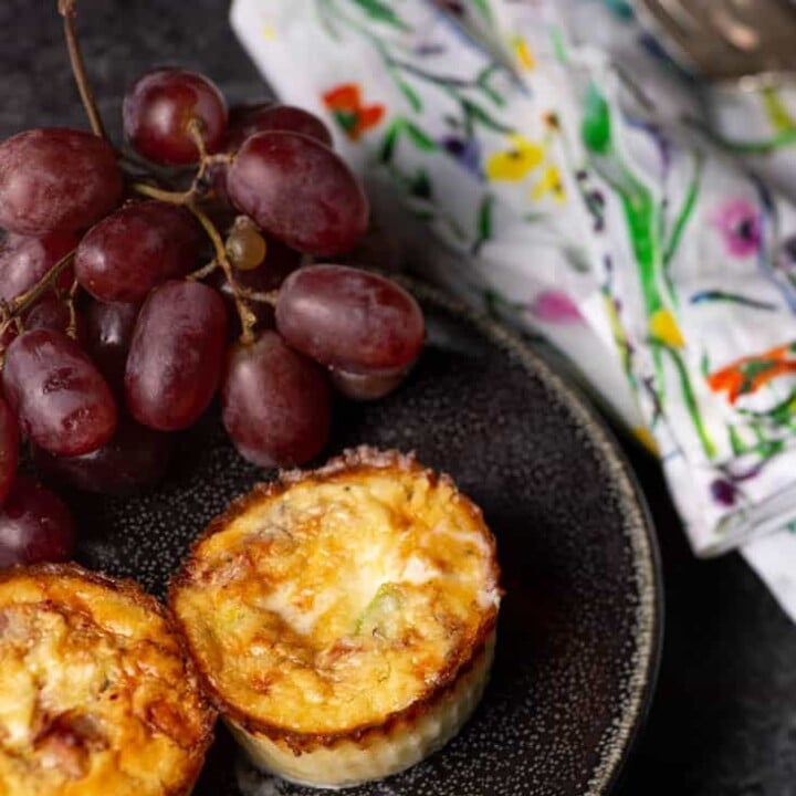 A black plate with two mini crustless quiches on them next to some red grapes