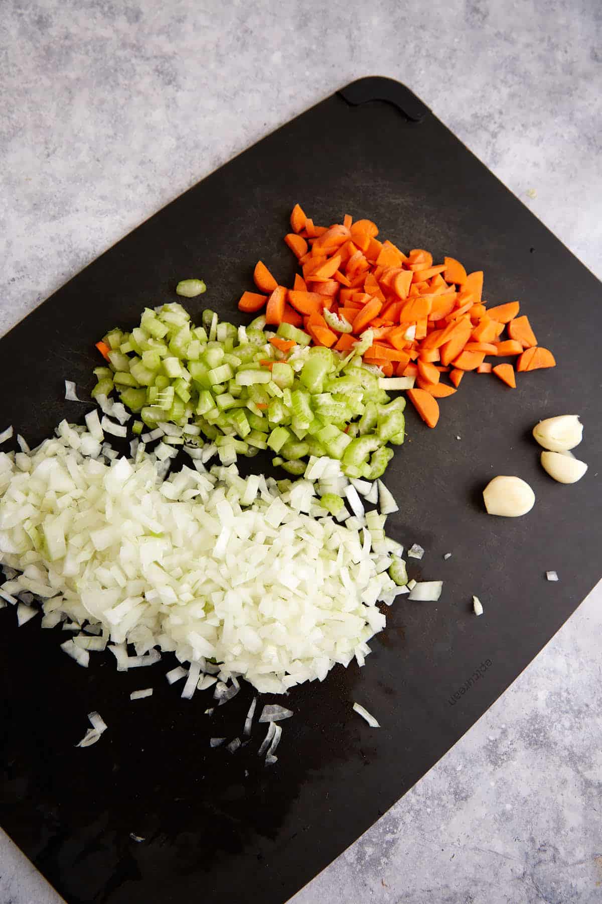 Onions, celery and carrots chopped on a cutting board.