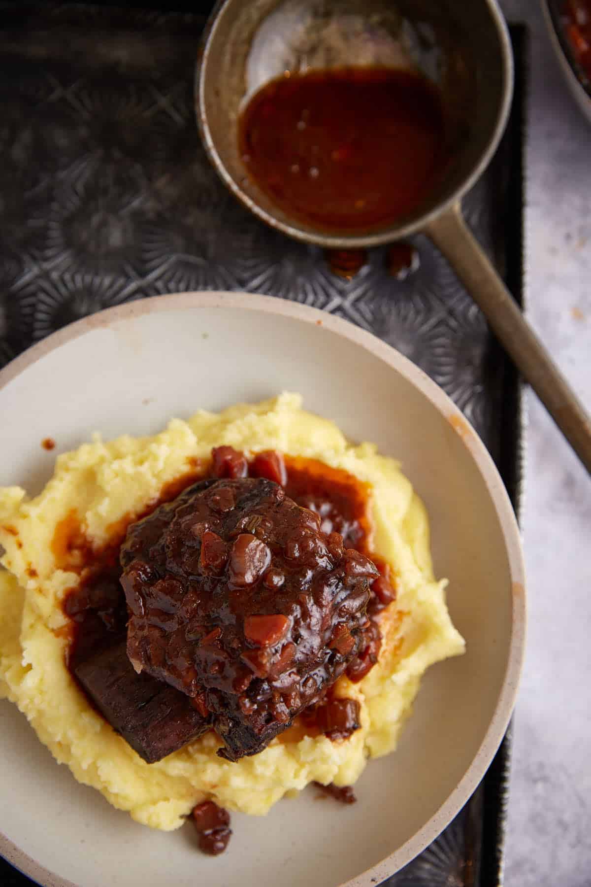 A braised short rib on a plate of mashed potatoes.