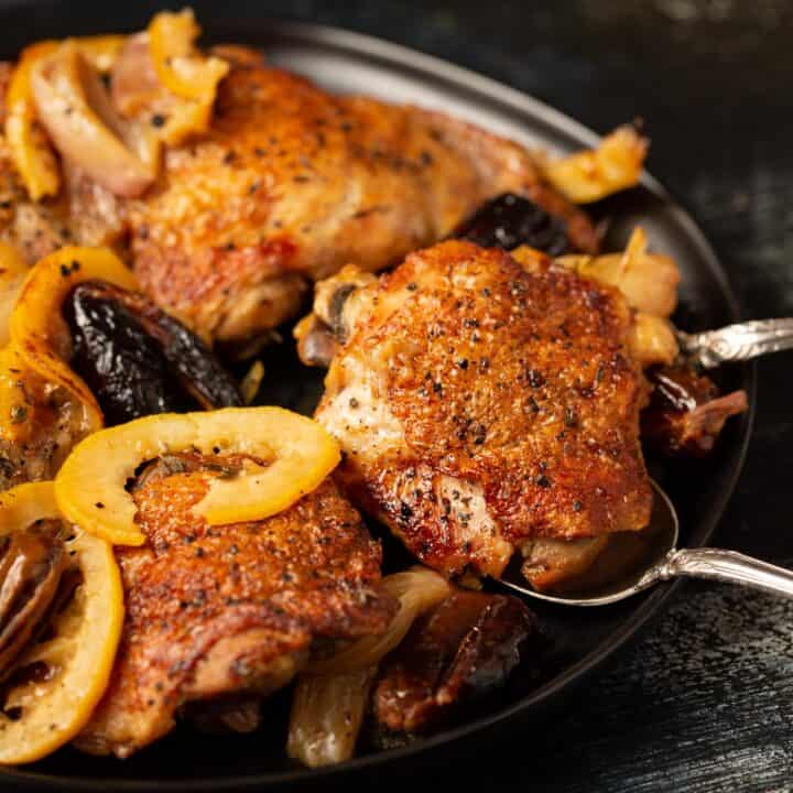 A chicken thigh with crispy skin being removed with a serving spoon.