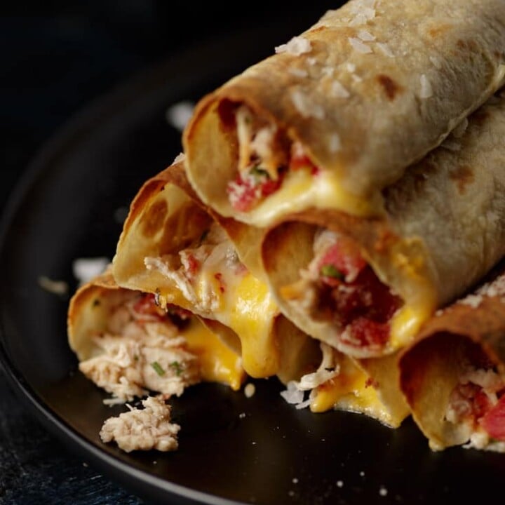 A platter of stacked baked chicken taquitos