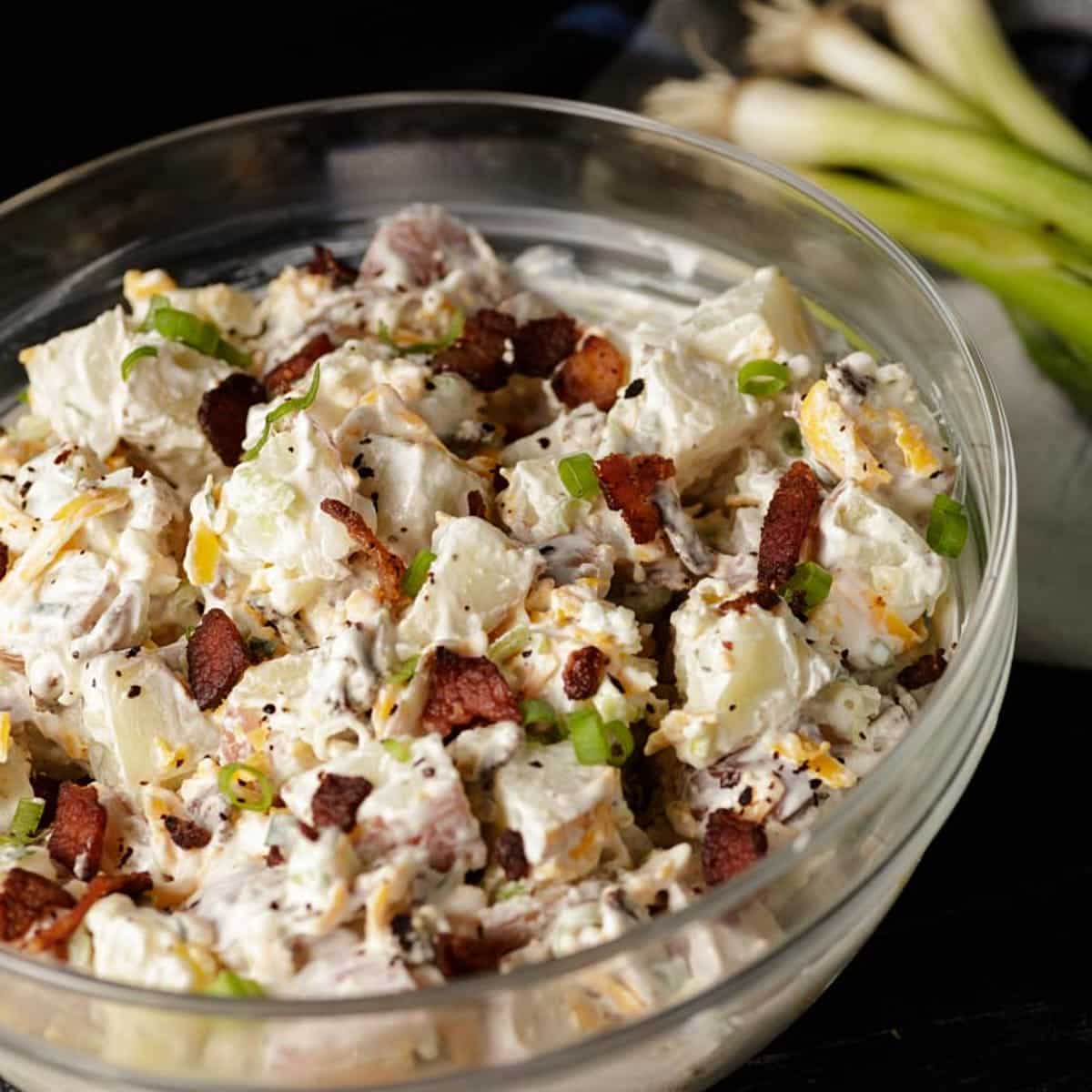 Southern style Ranch potato salad in a glass bowl next to green onions.
