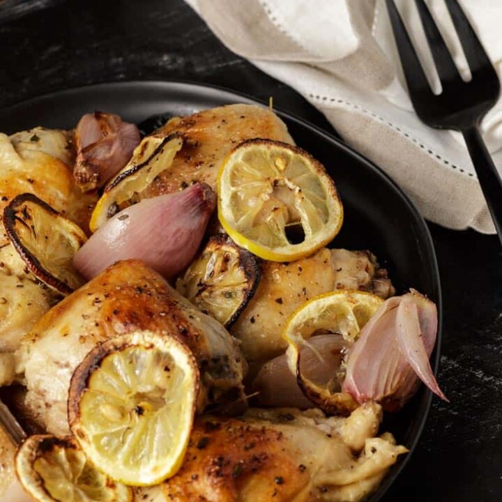 A platter of roasted chicken with lemons with a black fork
