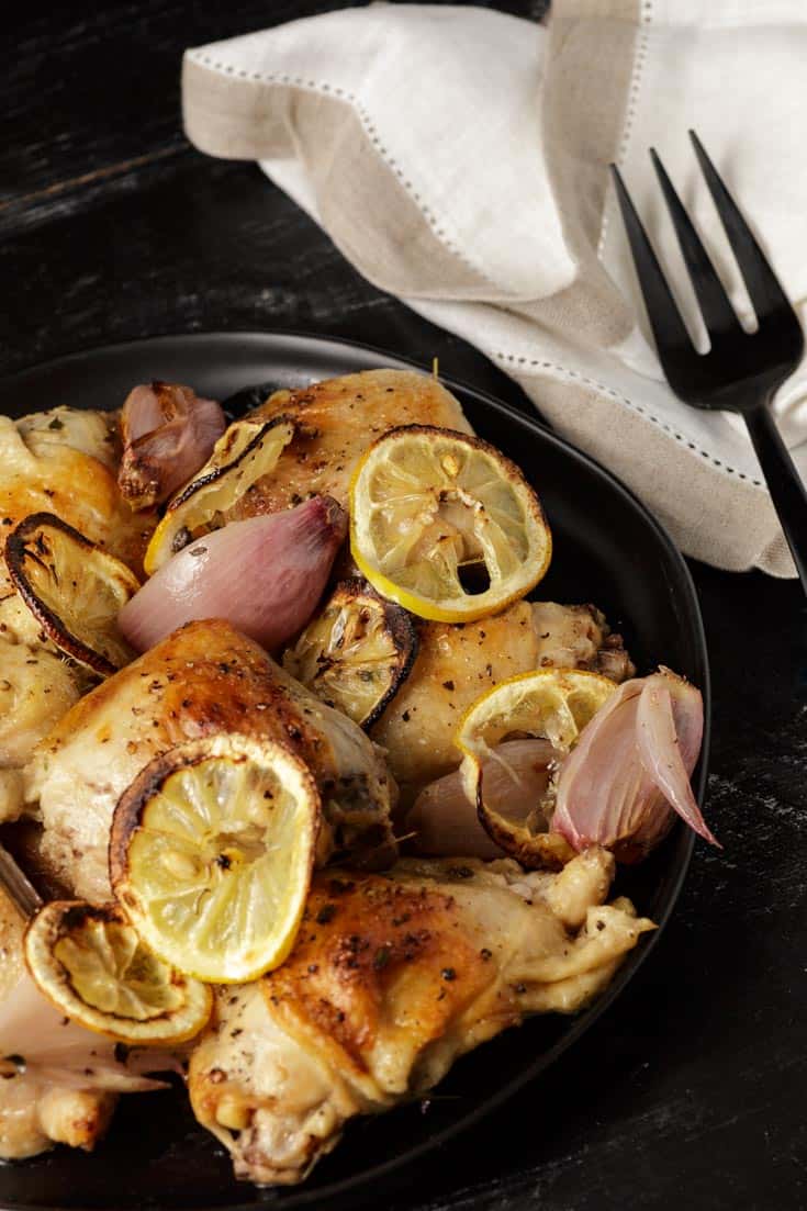 A platter of roasted chicken with lemons with a black fork