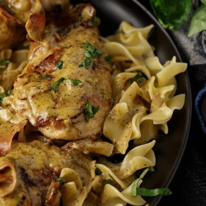 A black platter of prosciutto wrapped chicken over noodles